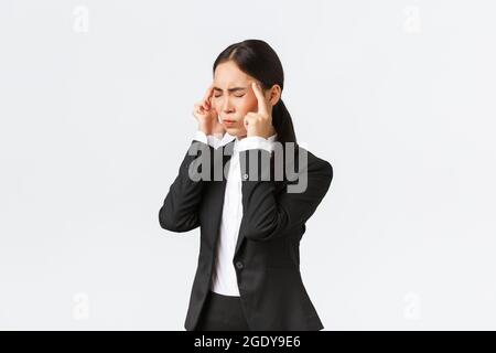 Profil de femme d'affaires asiatique en costume noir ayant la migraine, touchant les temples et grimacing de la sensation douloureuse dans la tête. Femme responsable de bureau Banque D'Images