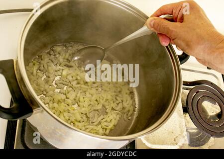 Faire frire l'oignon haché dans l'huile dans une casserole. La main d'une femme mélange l'oignon avec une cuillère. Le processus de cuisson de la viande avec des oignons. Banque D'Images