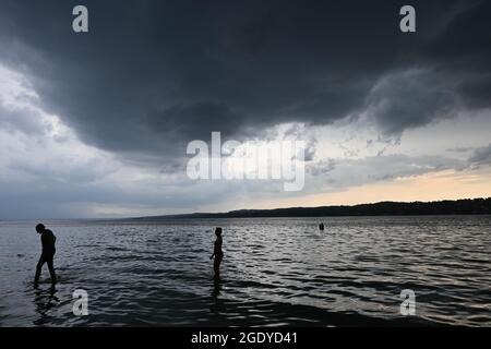Percha, Allemagne. 15 août 2021. Des nuages sombres pendent sur le lac Starnberg, dans lequel deux personnes sont debout. Credit: Katrin Requadt/dpa/Alay Live News Banque D'Images