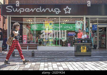 Belfast, Royaume-Uni. 18 juillet 2021. Une femme au téléphone passe devant la pharmacie SuperDrug et le magasin de beauté sur Ann Street à Belfast. Crédit : SOPA Images Limited/Alamy Live News Banque D'Images