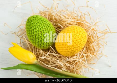 Œufs de pâques crochetés jaunes verts avec tulipe sur fond blanc Banque D'Images