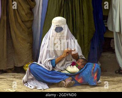 Une femme portant la burka complète tient son enfant dans ses armes sur le marché à Peshawar, au Pakistan. Banque D'Images