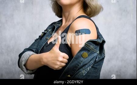 COVID-19 jeune femme vaccinée montrant le bras avec du plâtre. Une personne en bonne santé se fait le pouce après avoir reçu le vaccin contre le coronavirus. Concept de vaccination des personnes, dans Banque D'Images