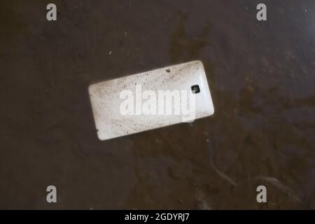 Téléphone mobile couché sur la chaussée dans la flaque Banque D'Images