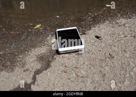 Téléphone mobile couché sur la chaussée dans la flaque Banque D'Images