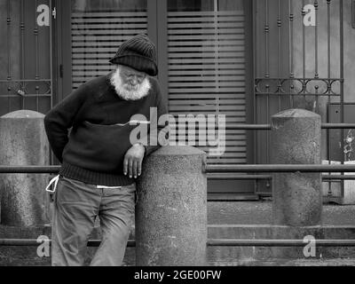 Une vieille tramp avec une barbe blanche est penchée contre le pilier en pierre d'une balustrade snoozing dans la vieille ville de Catane, Sicile Banque D'Images