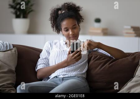 Une jeune femme afro-américaine se détende à la maison à l'aide d'un téléphone portable Banque D'Images
