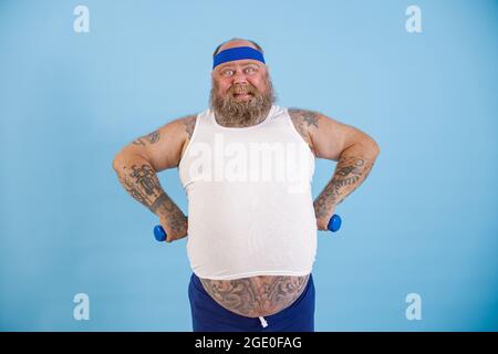 Heureux plumb homme avec de petits haltères tient les mains à la taille sur fond bleu clair Banque D'Images