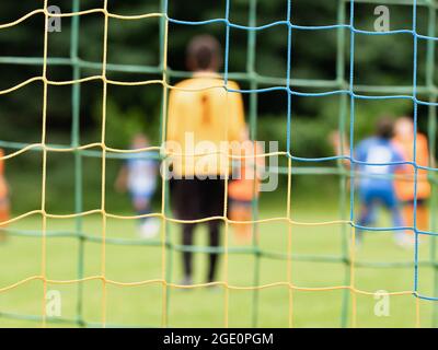 Vue à travers le filet de football. Le gardien de but recule lentement pendant l'attaque des adversaires. Vue abstraite Banque D'Images