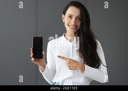Jeune femme tenant un téléphone portable et pointant vers lui avec l'index Banque D'Images
