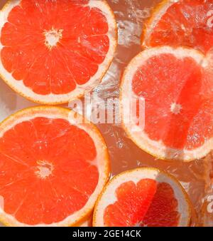 Vue rapprochée des tranches de pamplemousse rouge sur fond de limonade. Texture de la boisson fraîche douce d'été avec des bulles macro sur le mur de verre. Plat Banque D'Images