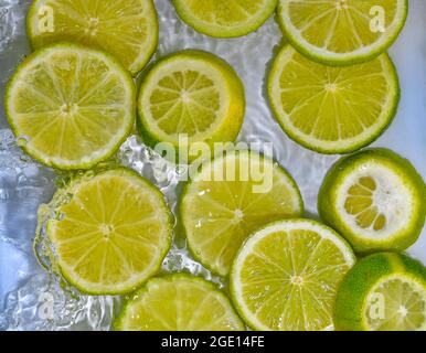 Elle limes les gros-plan dans le liquide avec des bulles. Tranches de limes vertes mûres dans l'eau. Gros plan sur des tranches fraîches de limes jaunes sur fond blanc Banque D'Images
