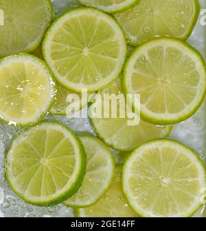 Elle limes les gros-plan dans le liquide avec des bulles. Tranches de limes vertes mûres dans l'eau. Gros plan sur des tranches fraîches de limes jaunes sur fond blanc Banque D'Images