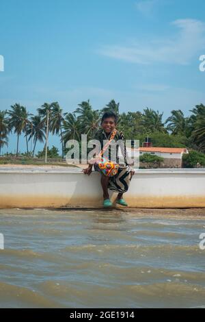 Riohacha, la Guajira, Colombie - Mai 30 2021: Jeunes indigènes Latin Boy Smiles assis sur et Old White Speed Boat Banque D'Images