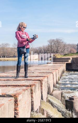 Femme adulte debout sur un chemin de briques dans le parc tenant une nacelle avec téléphone dans une journée ensoleillée. Banque D'Images