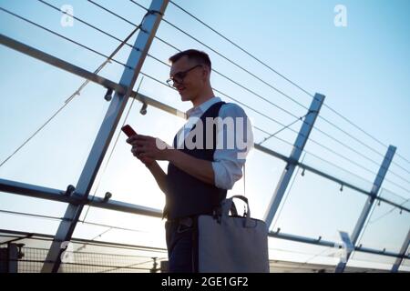 jeune homme avec un sac pour ordinateur portable lisant un message sur son smartphone Banque D'Images