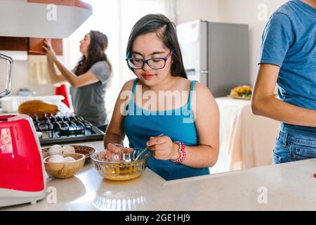 Adolescente mexicaine avec le syndrome de Down avec sa famille cuisiner dans la cuisine à la maison, dans le concept de handicap en Amérique latine Banque D'Images