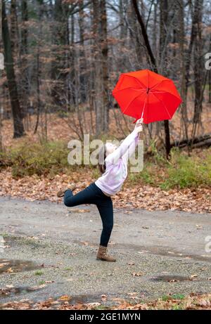 la jeune fille tient sur serré à un parapluie rouge vif comme le vent essaie du tirer loin Banque D'Images