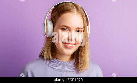 Bonne jeune femme dans le portrait de casque. Belle femme souriante avec une coiffure blonde Profitez de la musique de chanson dans un casque isolé au-dessus de violet Banque D'Images