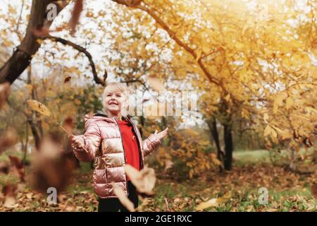 Petite fille blonde joue avec des feuilles d'automne jaunes dans le jardin, sourire, a du plaisir Banque D'Images