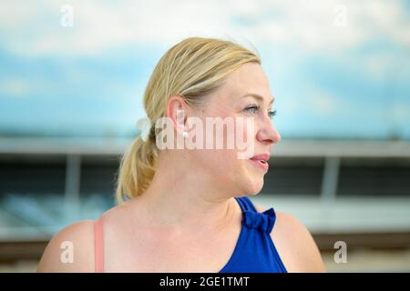 Blonde aux yeux bleus d'âge moyen femme profil tête portrait regardant de côté comme elle pose à l'extérieur en plein soleil d'été dans un élégant haut bleu à l'épaule Banque D'Images