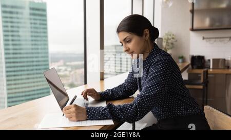 Femme indienne travaillant avec un ordinateur portable effectuant des corrections dans le document Banque D'Images