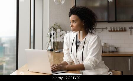 Une femme africaine pensive distraite d'un ordinateur portable et regarde à distance Banque D'Images