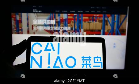 Personne tenant un téléphone portable avec le logo de la société Cainiao Smart Logistics Network Limited à l'écran en face de la page Web. Mise au point sur l'affichage du téléphone. Banque D'Images