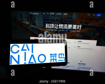 Personne tenant un téléphone portable avec le logo de la société Cainiao Smart Logistics Network Ltd à l'écran en face de la page Web d'affaires. Mise au point sur l'affichage du téléphone. Banque D'Images