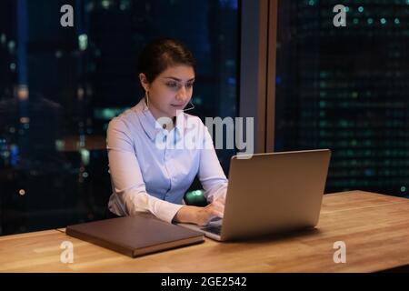 Femme indienne qui envoie des SMS sur un ordinateur travaillant jusque tard dans le bureau Banque D'Images