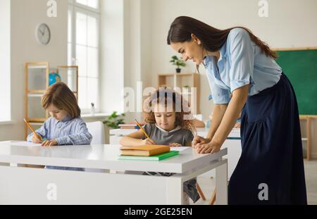 Un professeur caucasien amical aide les élèves juniors à accomplir correctement la tâche de l'école. Banque D'Images