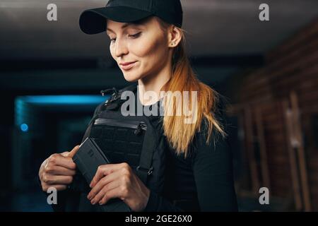 Jolie dame dans un gilet à l'épreuve des balles de chargement de son arme Banque D'Images