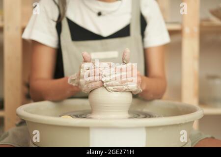 Crop anonyme femme maître en tablier façonnant vase d'argile sur roue de poterie rotative tout en travaillant dans studio professionnel Banque D'Images