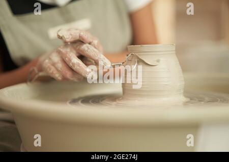 Rognez l'artisan anonyme en utilisant l'outil de boucle pour enlever l'excès d'argile tout en formant un vase d'argile humide sur la roue de poterie dans le studio d'art en céramique Banque D'Images