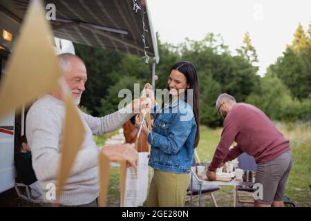 Famille de multi-génération préparant la fête en voiture en plein air en camping, voyage de vacances en caravane. Banque D'Images