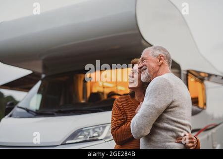 Couple senior debout et embrassant à l'extérieur au crépuscule, voyage de vacances en caravane. Banque D'Images