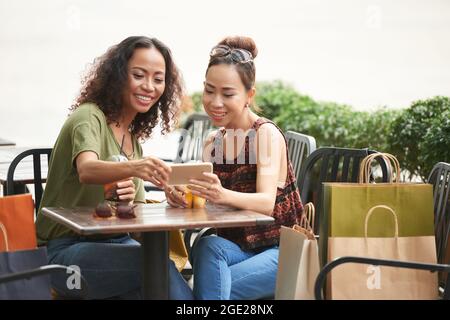 Jeune femme souriante montrant des photos sur un smartphone à un ami lorsqu'il se rencontre à une table de café Banque D'Images