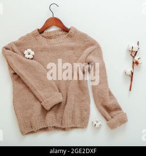 Pull beige tricoté sur cintre avec fleurs en coton. Pull en coton à motif mouches à plat et motif brindille de coton sur fond blanc. Chaud et élégant hiver Banque D'Images
