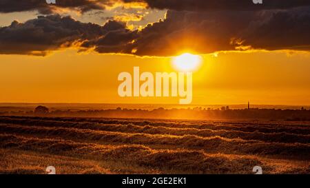 Caythorpe, Lincolnshire, Royaume-Uni. Coucher de soleil pendant la récolte sur un terrain de chaume en direction du village Banque D'Images