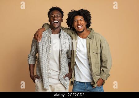 Portrait de deux hommes noirs heureux embrassant tout en posant sur le fond beige Banque D'Images