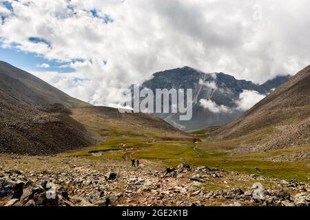 Vallée de montagne avec un passage entre les montagnes et une grande montagne à la fin. Nuages bas sur la montagne. Plusieurs touristes vont le long du trai Banque D'Images