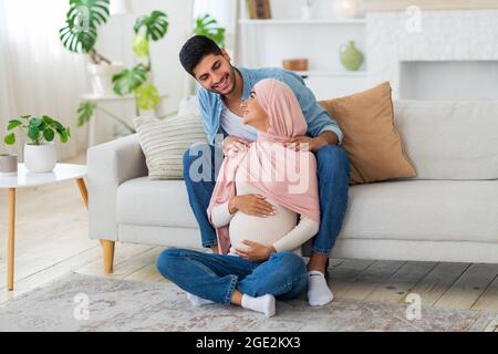 Un mari arabe heureux fait un massage des épaules pour sa femme musulmane enceinte, l'aidant à se détendre les muscles du dos Banque D'Images
