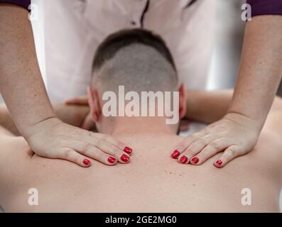 Gros plan des mains d'un massothérapeute féminin dans le processus de pétrissage et de massage du dos masculin. Banque D'Images