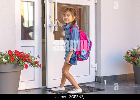 Une petite fille avec un sac à dos, une écolière ouvre les portes de l'école. Banque D'Images