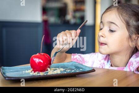 Petite fille mignonne à manger de la mousse au chocolat en forme de cerise, un dessert français avec une base de biscuits, du glaçage et des fruits. Banque D'Images