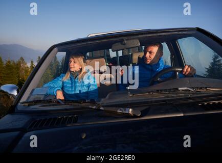 Charmante femme voyageur appréciant la beauté de la nature et souriant tandis que l'homme conducteur gardant les mains sur le volant et conduisant la voiture. Jeune couple Banque D'Images