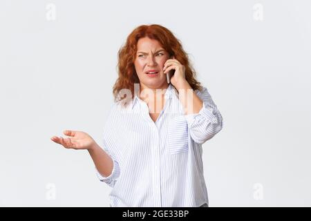 Frustrée et mécontente, confuse et grognante femme d'âge moyen haussant les épaules et craquant dégoûtée en parlant sur téléphone portable de quelque chose de terrible Banque D'Images