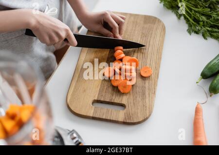 vue partielle de la femme coupant la carotte brute près de concombres frais sur la table de cuisine Banque D'Images