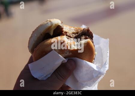 Double cheeseburger à la main avec bouchée, hamburger de restauration rapide, promenade en bord de mer Barry Island, Galles du Sud, 2021 Banque D'Images