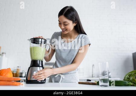 joyeuse femme asiatique préparant un smoothie de légumes dans un shaker électrique Banque D'Images